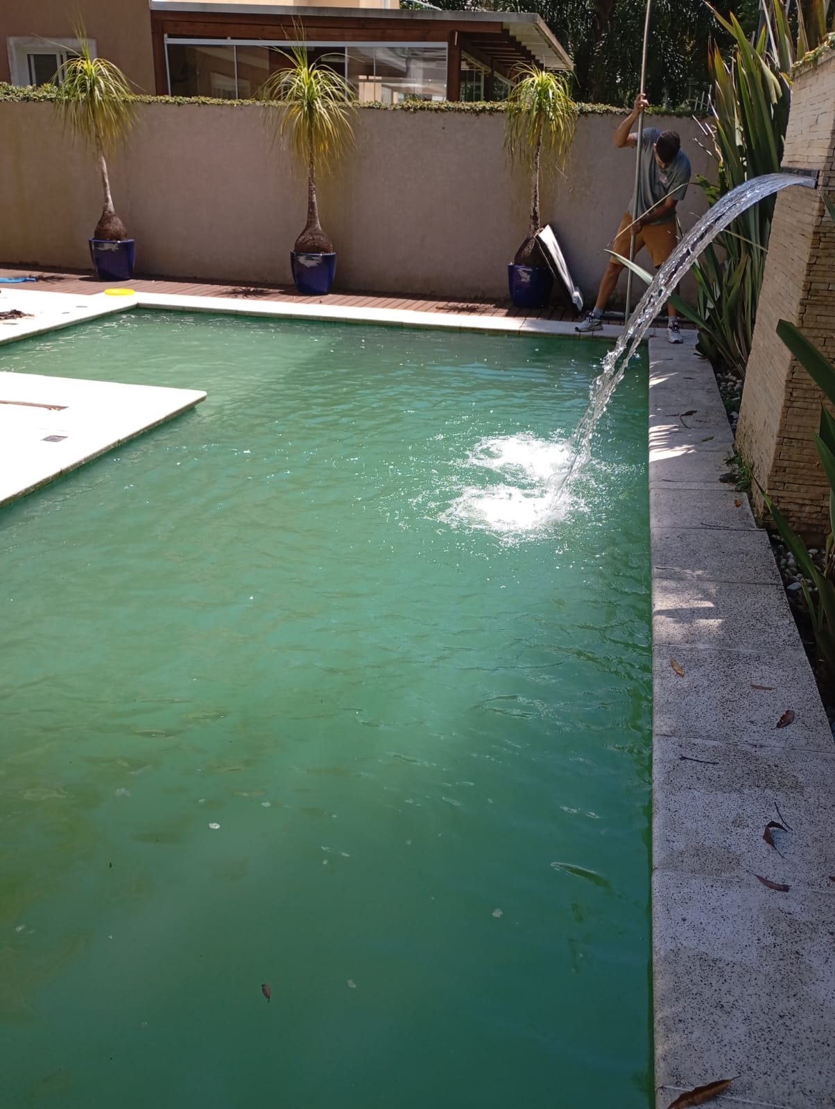 Técnico limpando a piscina retangular com cabo, cascata ligada